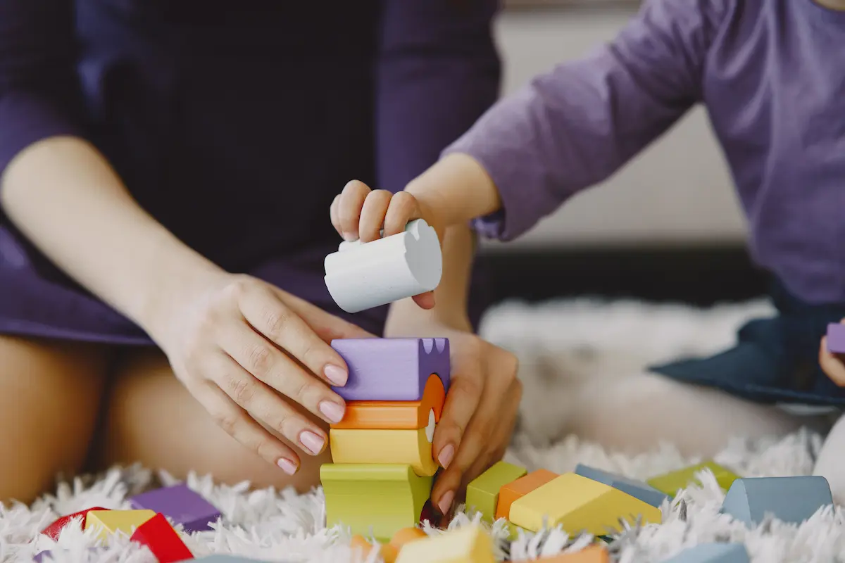 Niño pequeño jugando con bloques o materiales educativos acompañado por un adulto, representando una sesión de estimulación del desarrollo.